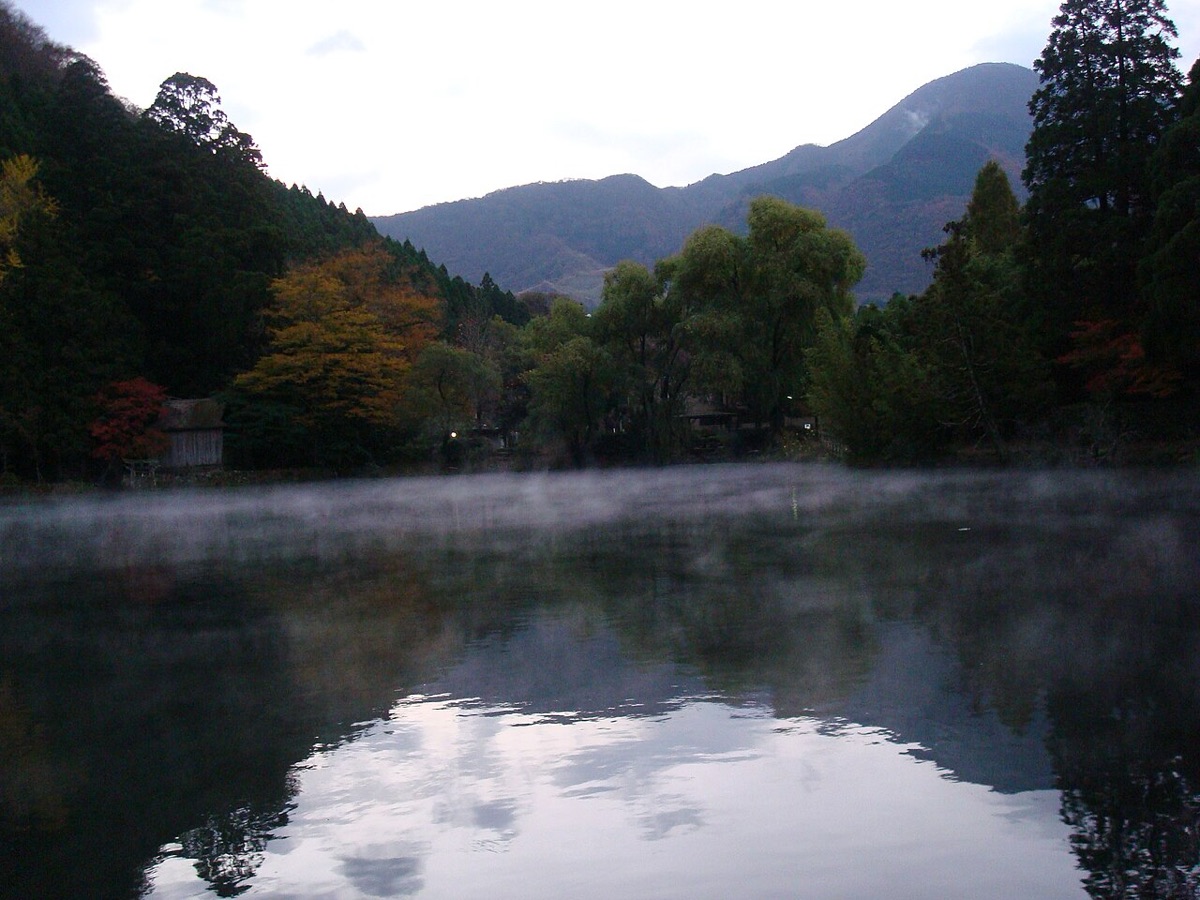 秋天清晨由布院金鱗湖湖面飄著晨霧,背景是由布岳山稜與紅葉