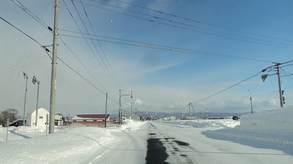 A snow-covered and icy winter road in Hokkaido with marker poles at the roadside