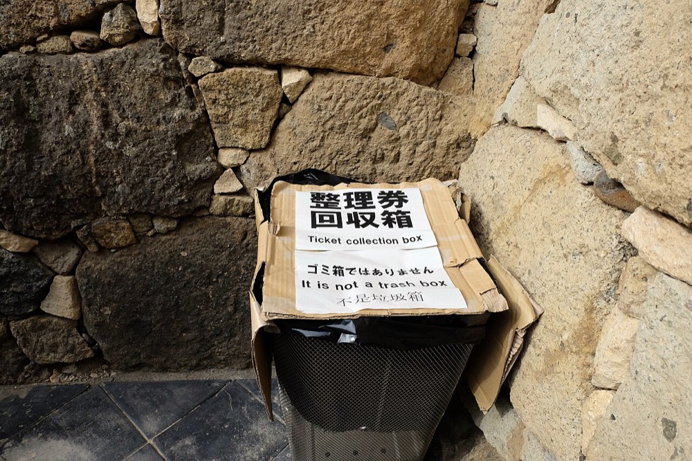 A ticket-collection box beside a stone wall with a sign saying it is not a trash can