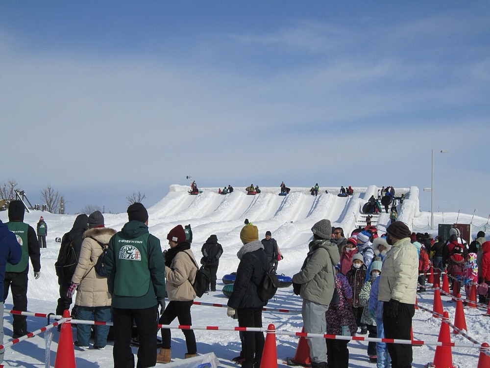 A crowd lined up at the snow slide, with people at the top sitting on tubes ready to slide down