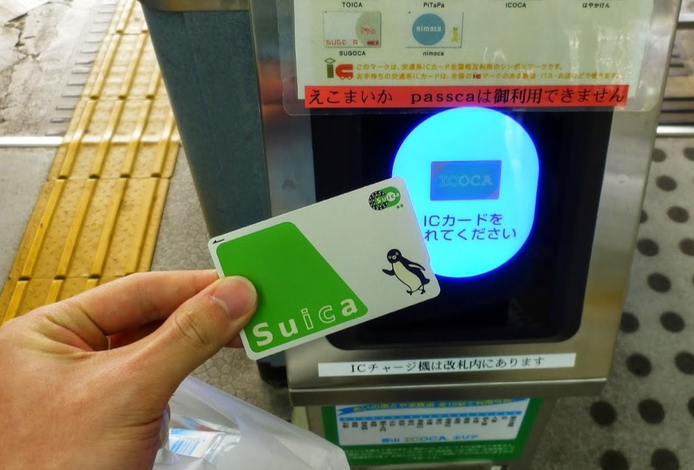 A hand holding a Suica card, about to tap it on a ticket gate