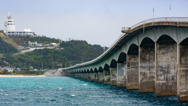 沖繩自駕必經的古宇利大橋橫跨翡翠色海面，遠方是古宇利島與海洋塔